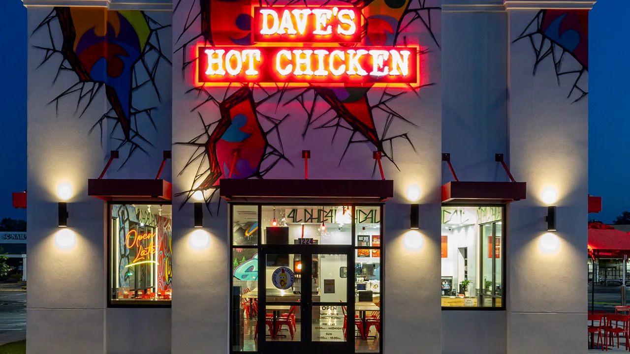 Modern Front entrance of Dave’s Hot Chicken on Woodruff Rd in Greenville, SC, illuminated by bright neon signage and bold murals.