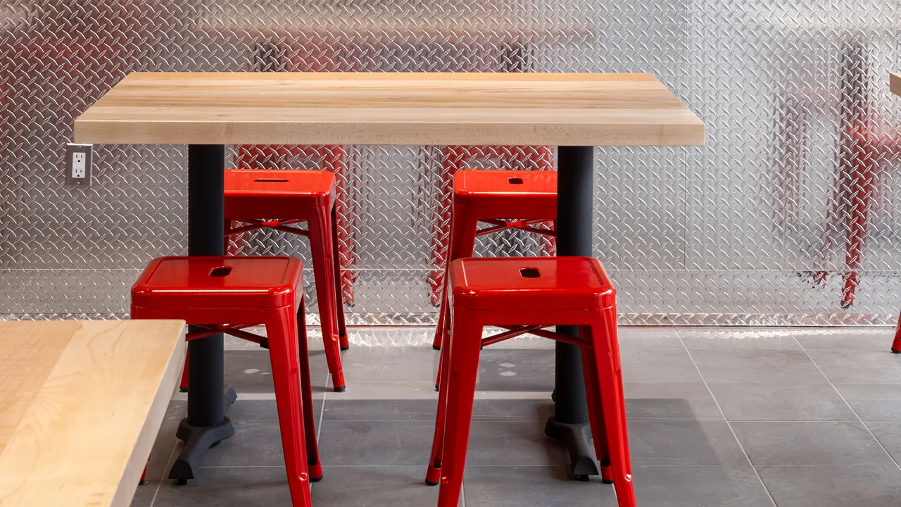 Interior view of seating area with red stools and wooden tables at Dave's Hot Chicken on Yonge & Dundas, Toronto, ON.