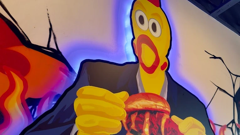 A hand painted wall mural inside a Dave's Hot Chicken restaurant on Western Avenue in Los Angeles. The mural features the Dave's rubber chicken mascot holding a spicy chicken slider.