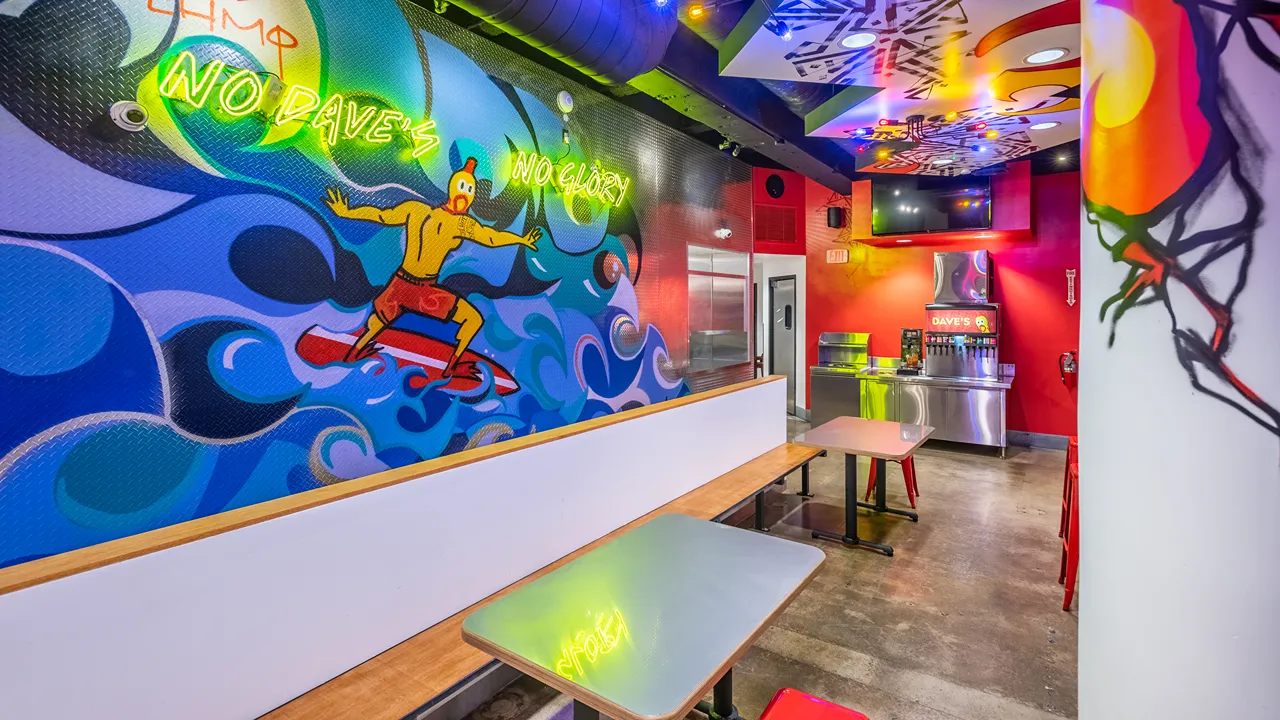 Indoor seating area with colorful surfing-themed wall art and neon lights at Dave's Hot Chicken on Garnet Ave in Pacific Beach, San Diego, CA.