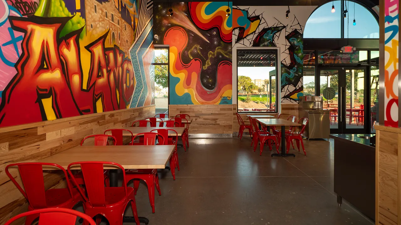 Indoor dining area with colorful Alamo mural and red chairs at Dave's Hot Chicken, La Picosa on SE Military Drive and South New Braunfels Avenue, San Antonio, TX.