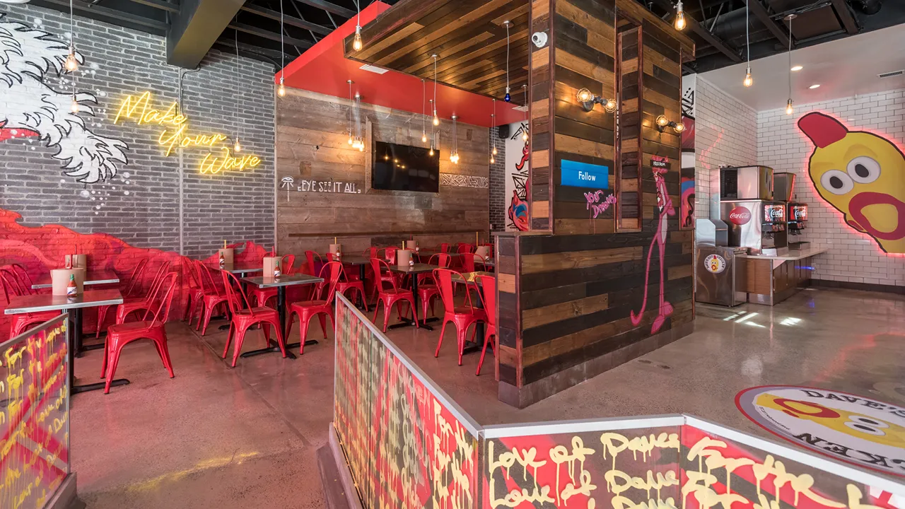 Dining area with colorful wall art, red metal chairs, and wooden tables at Dave's Hot Chicken on Lankershim Blvd, North Hollywood.