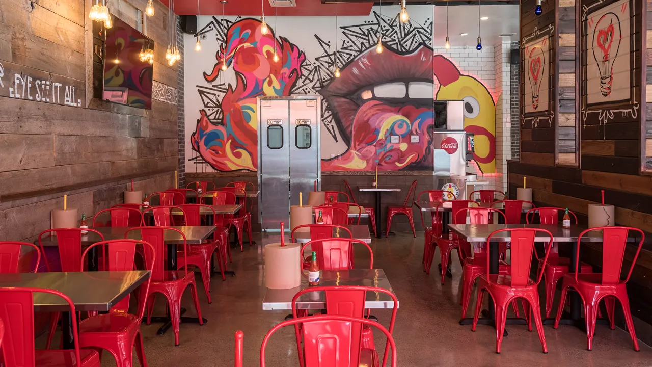 Dining area with colorful wall art, red metal chairs, and wooden tables at Dave's Hot Chicken on Lankershim Blvd, North Hollywood.