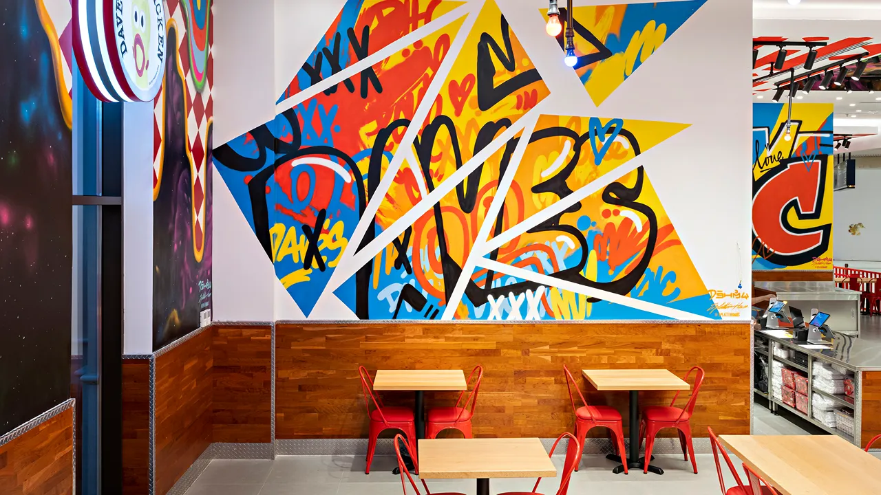 Vibrant geometric wall mural inside Dave’s Hot Chicken at Place Vendôme Mall, Lusail City, near Doha, Qatar, with stylish red seating.