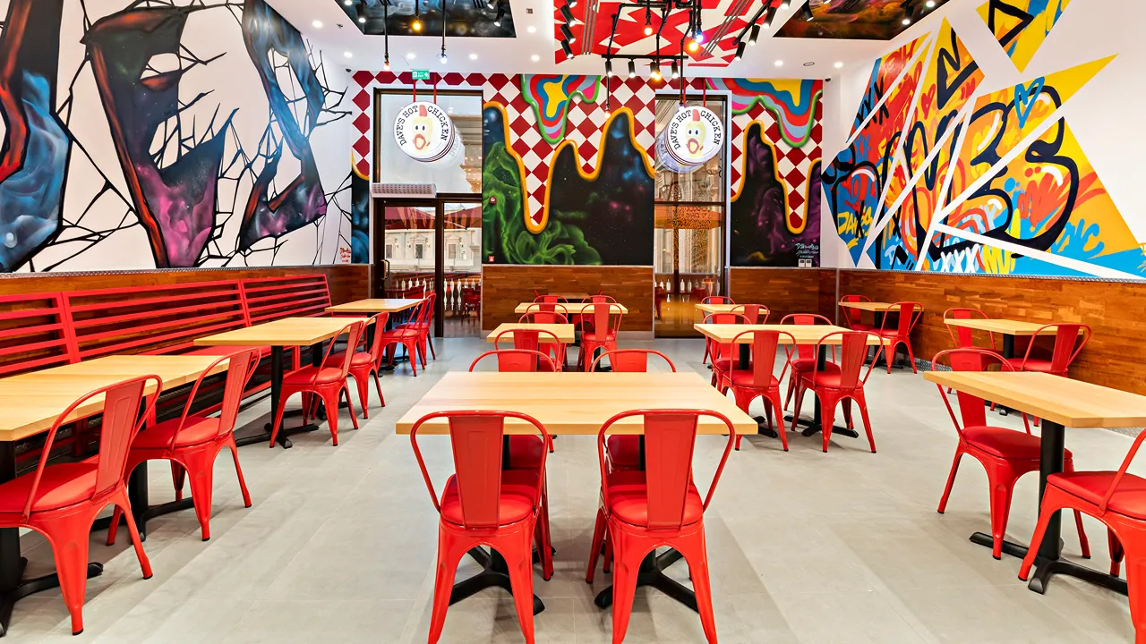 Spacious seating area inside Dave’s Hot Chicken at Place Vendôme Mall, Lusail City, near Doha, Qatar, with colorful wall art and red chairs.