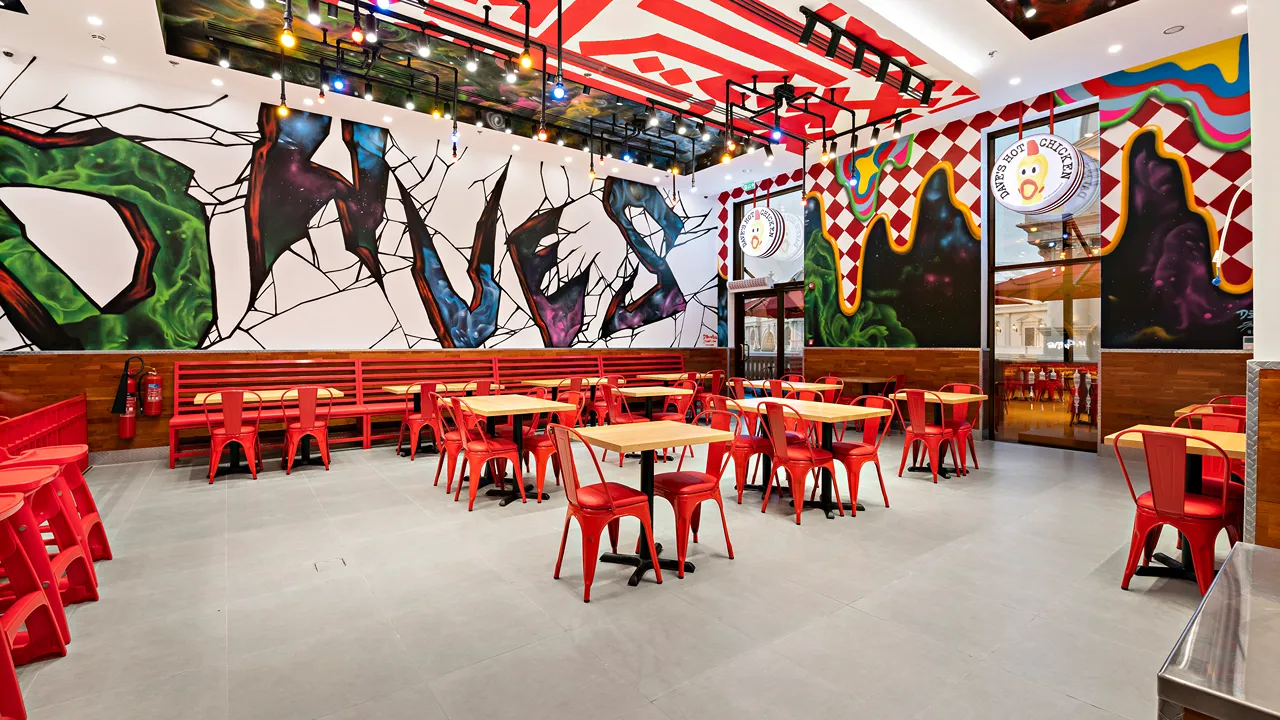 Wide-angle view of Dave’s Hot Chicken seating area at Place Vendôme Mall in Lusail City, near Doha, Qatar, featuring bold murals and modern red chairs.