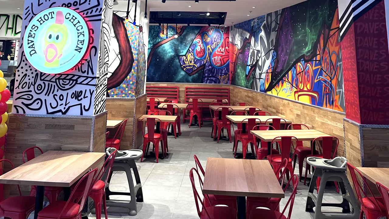 Spacious dining area with red chairs and artistic murals at Dave's Hot Chicken in Villagio Mall, Doha, Qatar, on Al Waab St.