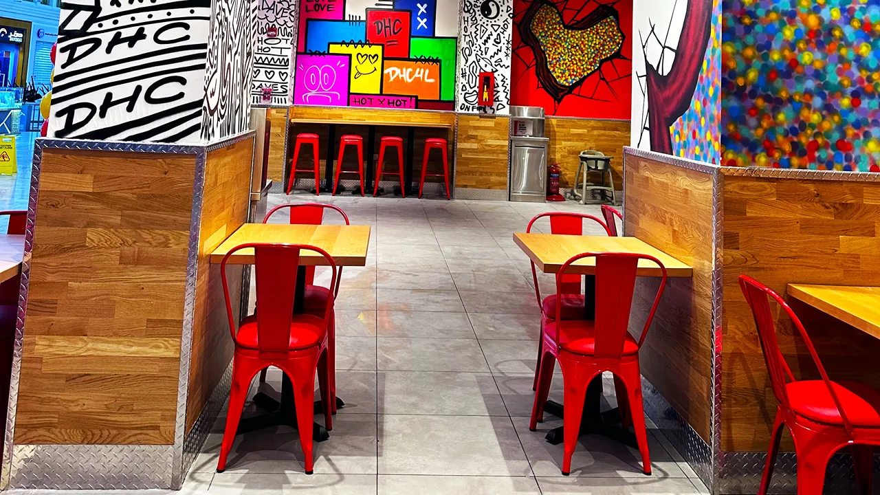Indoor seating area with red chairs and colorful wall murals at Dave's Hot Chicken in Villagio Mall, Doha, Qatar, on Al Waab St.