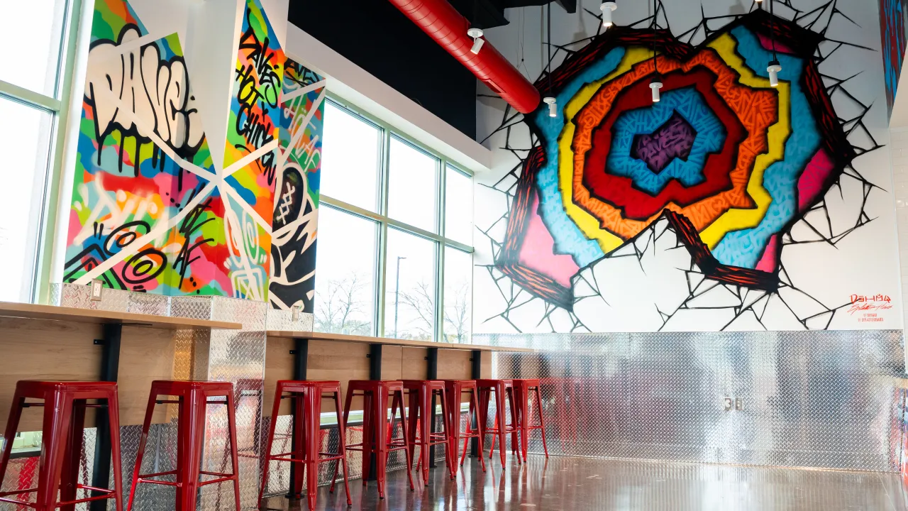 Interior view of Dave's Hot Chicken on 3022 E 53rd St, Davenport, IA, showcasing vibrant murals and red bar stools.