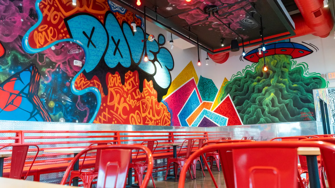 Interior view of Dave's Hot Chicken at 3022 E 53rd St, Davenport, IA, showcasing vibrant murals and red seating.