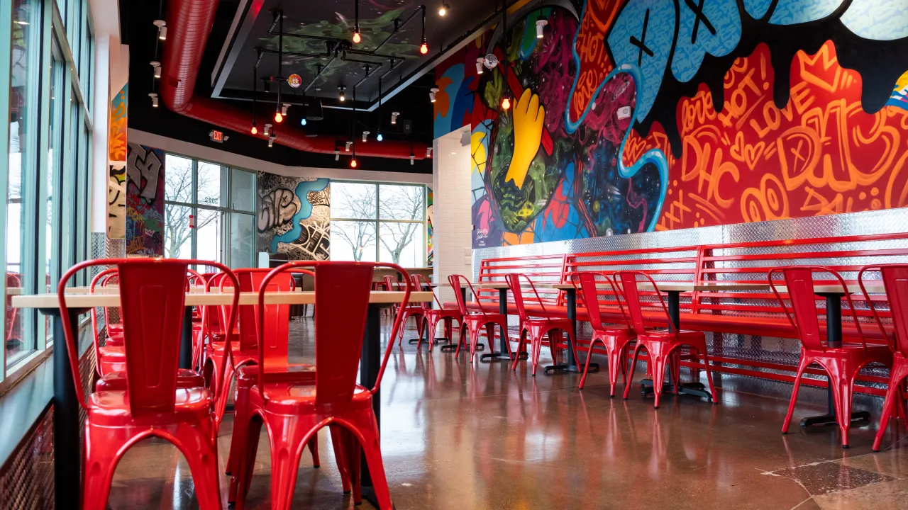 Interior view of Dave's Hot Chicken on 3022 E 53rd St, Davenport, IA, featuring vibrant murals and red metal furniture.