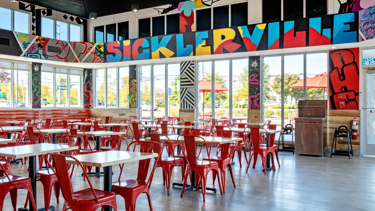 Interior view of Dave’s Hot Chicken in Sicklerville, NJ, showcasing vibrant 'Sickerville' mural and the dining area.