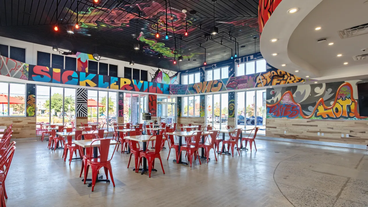 Interior view of Dave's Hot Chicken in Sicklerville, NJ, showcasing vibrant murals and red seating.