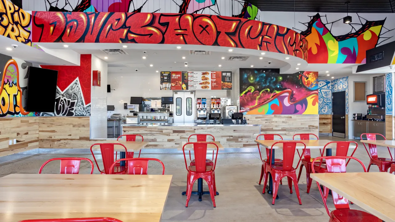 Interior view of Dave's Hot Chicken in Sicklerville, NJ, featuring vibrant murals and red chairs.