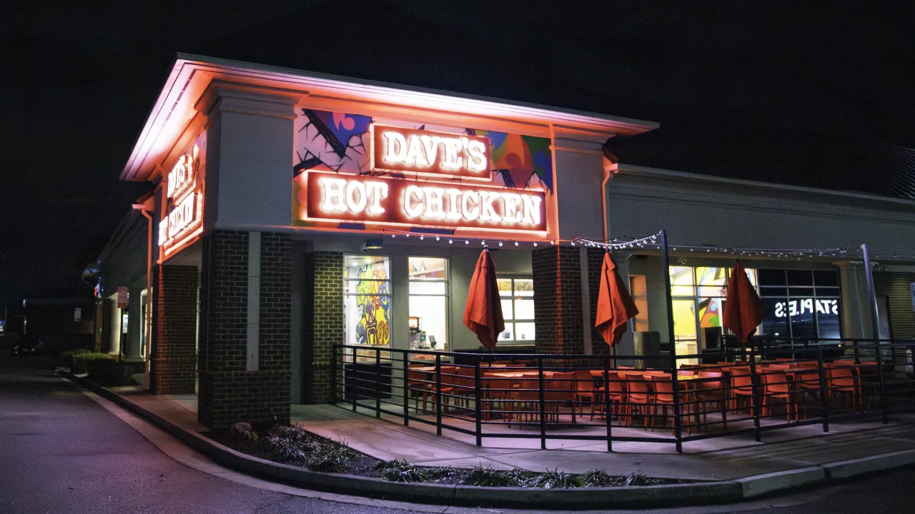 Exterior view of Dave's Hot Chicken at 11525 W. Broad St, Richmond, VA, showcasing bright signage and red umbrellas.