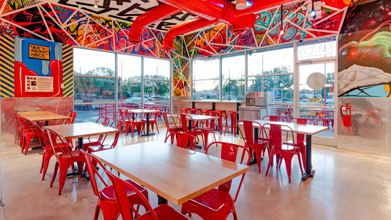 Interior view of Dave's Hot Chicken on Cherry Rd, Rock Hill, SC, showcasing vibrant murals and red metal seating.