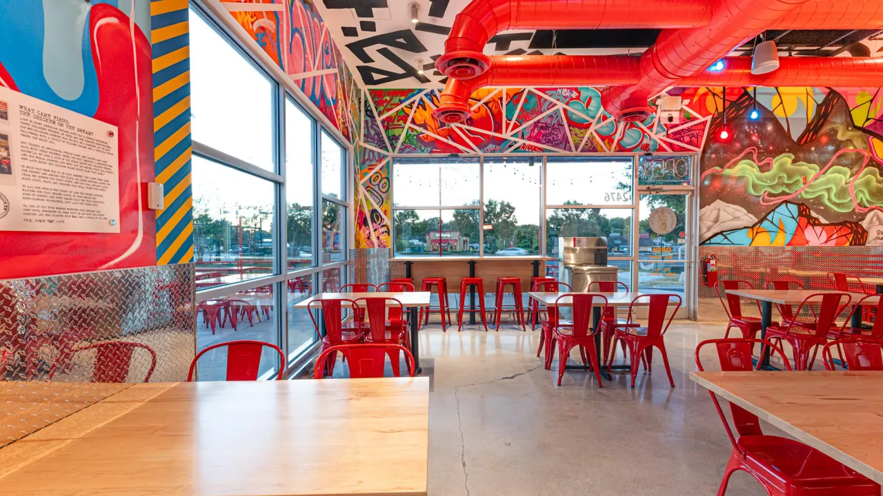 Interior shot of Dave's Hot Chicken on Cherry Rd, Rock Hill, SC, showcasing vibrant murals and modern red seating.