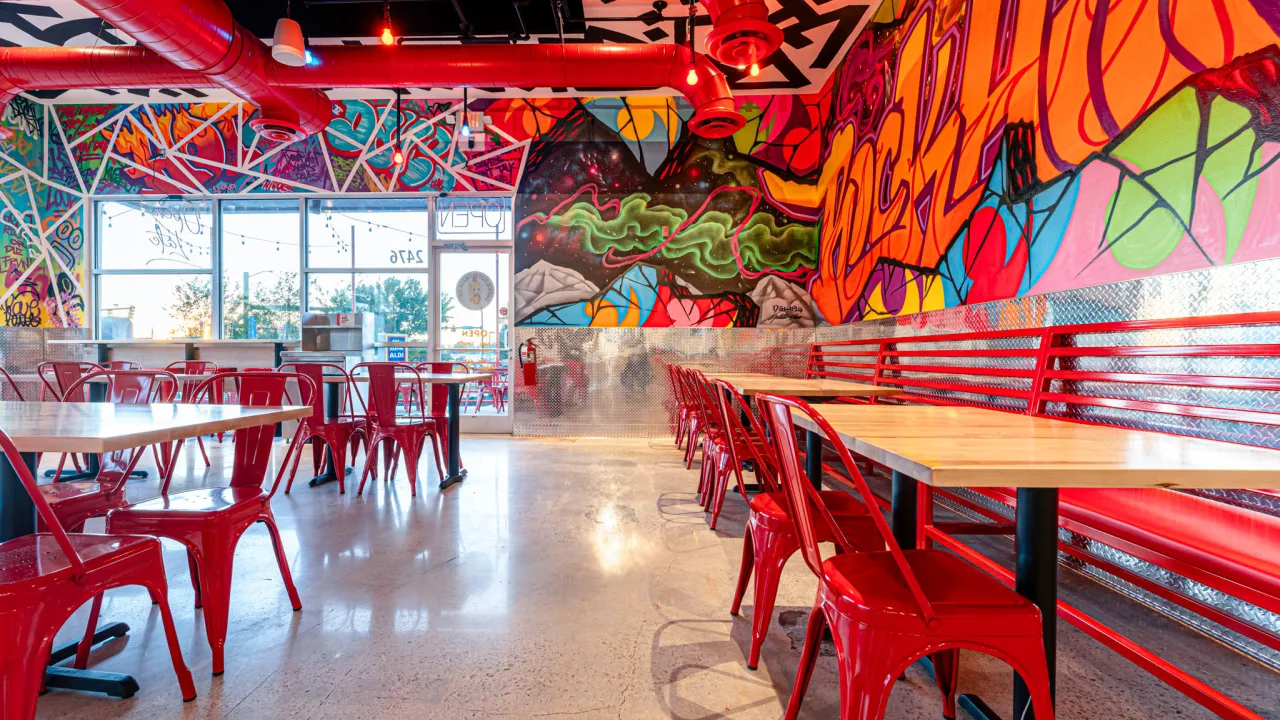 Interior view of Dave's Hot Chicken on Cherry Rd, Rock Hill, SC, featuring vibrant murals and red metal seating.