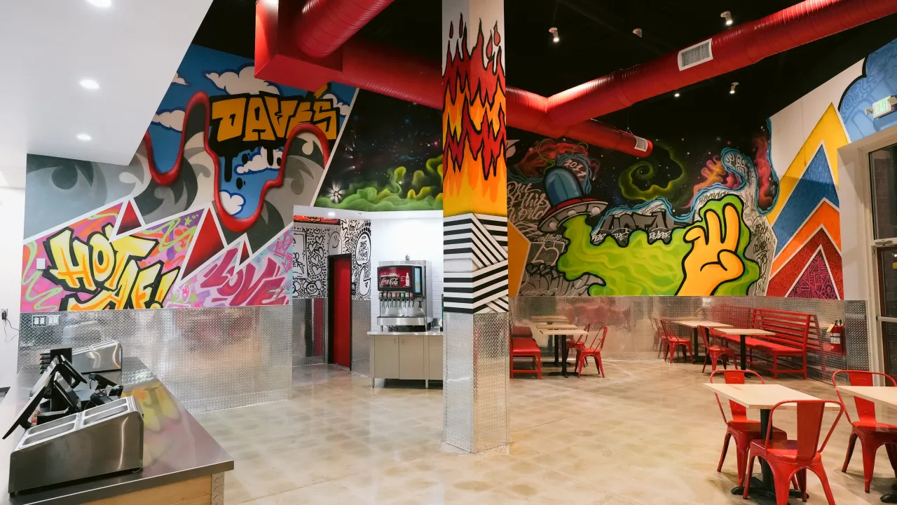 Interior view of Dave's Hot Chicken in Columbia, MD, showcasing vibrant murals and red seating.