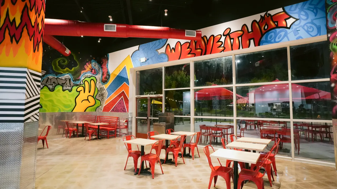 Interior view of Dave's Hot Chicken in the Columbia Crossing Shopping Centre, Columbia, MD, showcasing large windows, vibrant murals and red seating.