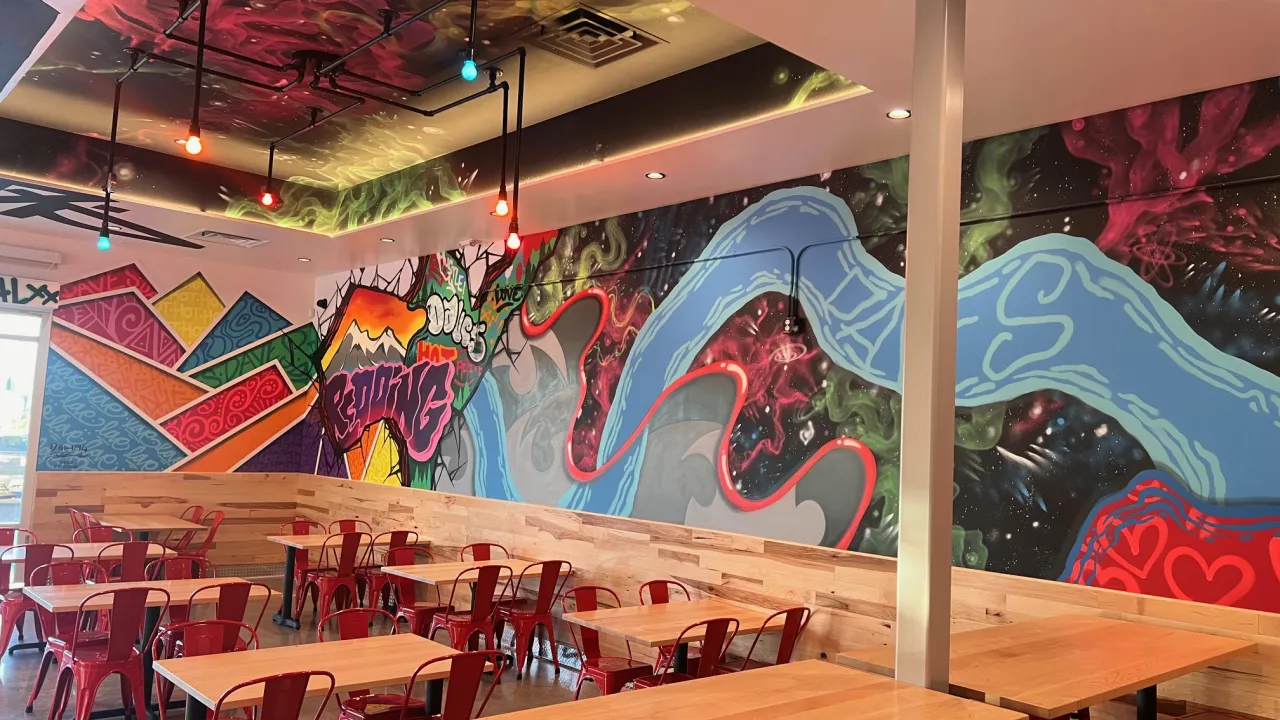 Interior view of Dave's Hot Chicken on Dana Dr, Redding, CA, showcasing vibrant murals and red metal chairs.