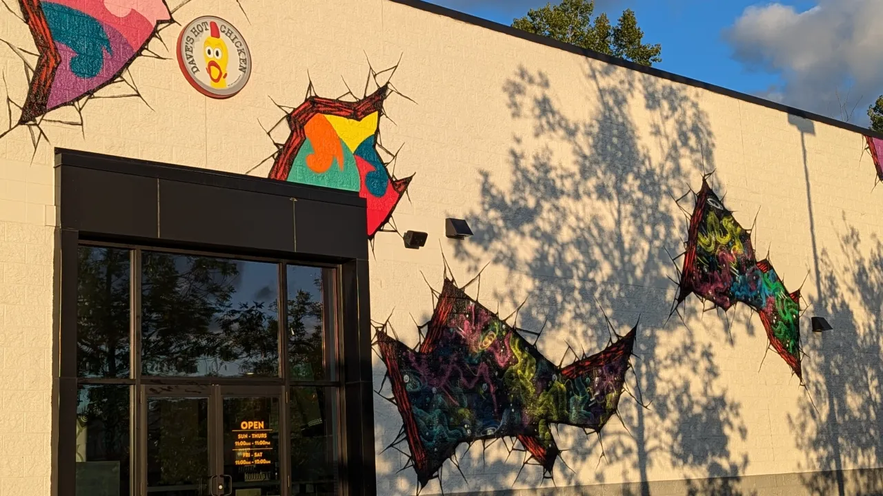 Exterior view of Dave's Hot Chicken on Dorset St, South Burlington, VT, showcasing vibrant murals and open hours signage.