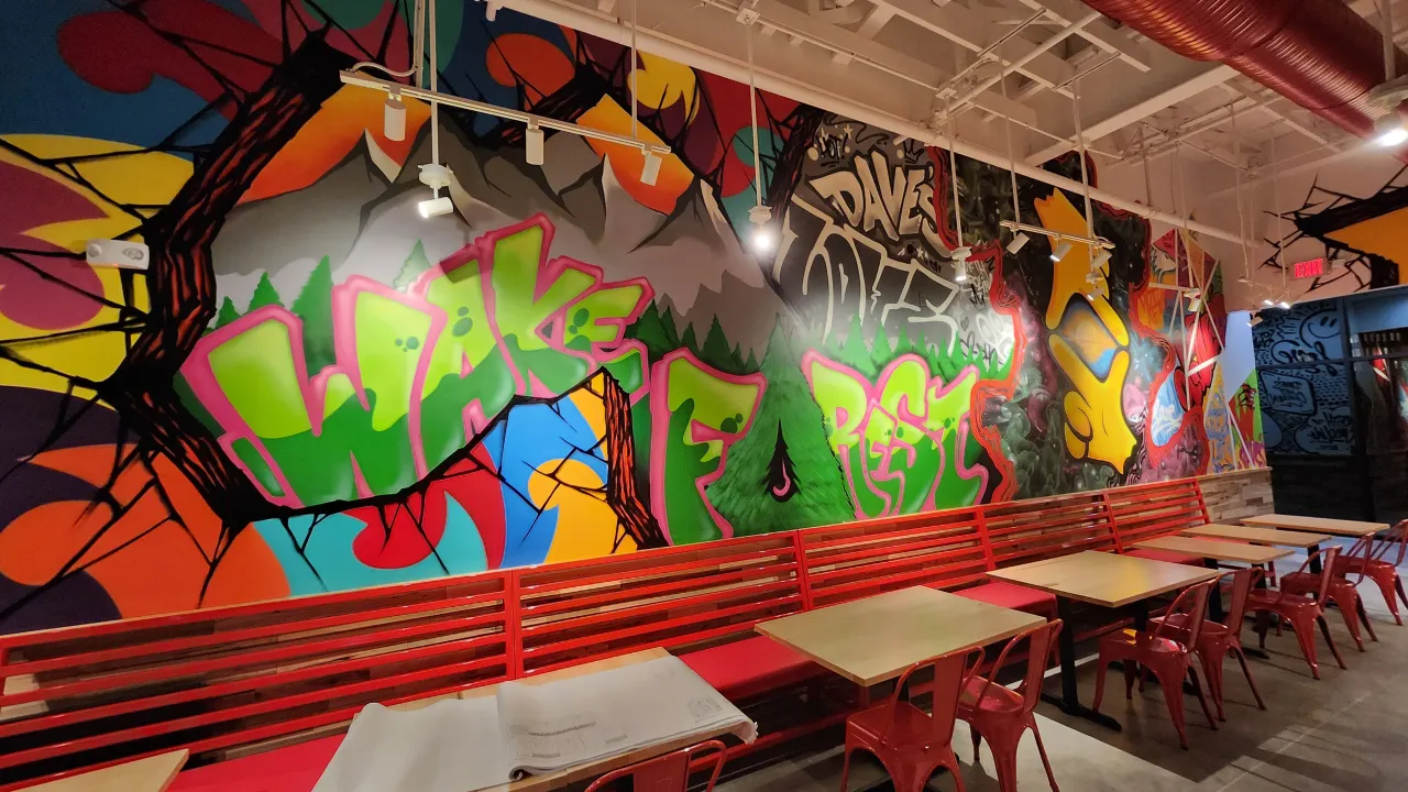 Interior view of Dave's Hot Chicken in Wake Forest, NC, showcasing vibrant murals and red seating.