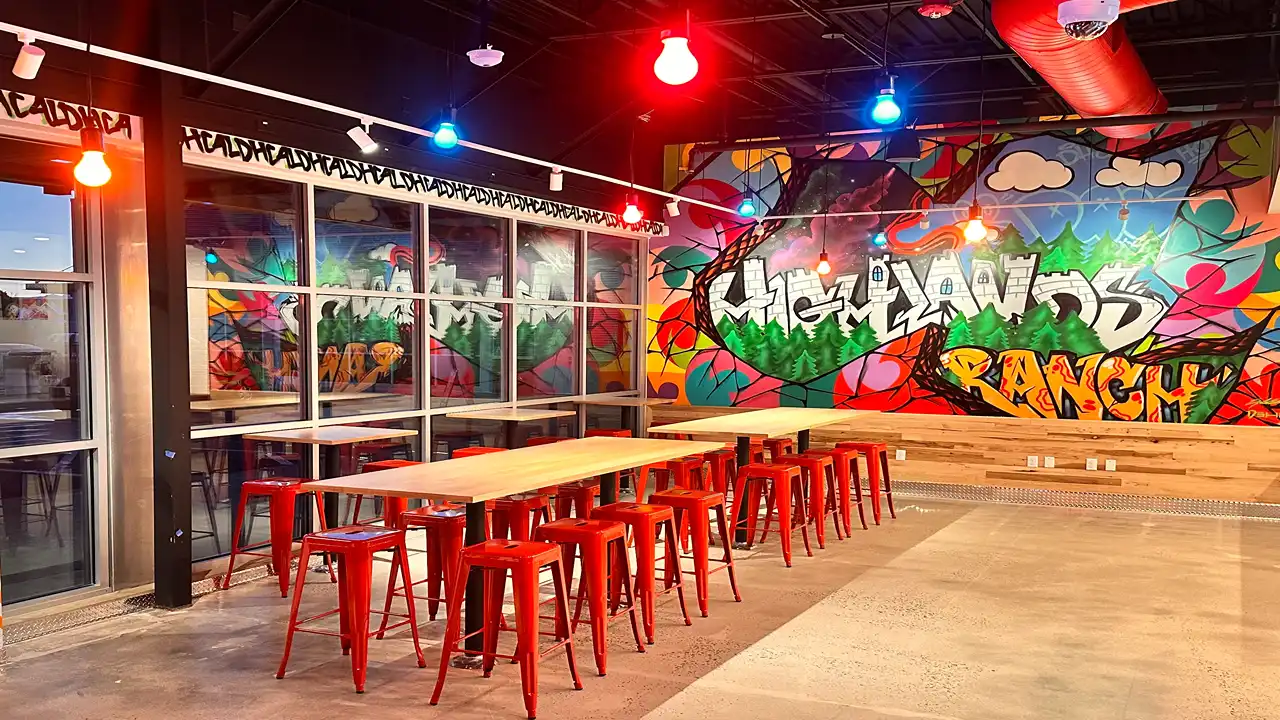 Bright dining area with modern red chairs and a mural of Highlands Ranch at Dave's Hot Chicken on Mayberry Dr, CO.