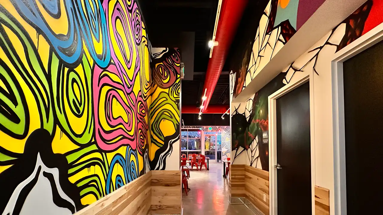 Unique hallway art with swirling patterns and vibrant designs leading to the dining area at Dave's Hot Chicken, Highlands Ranch, CO.