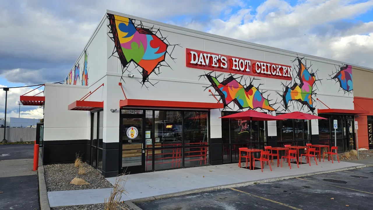 Exterior view of Dave's Hot Chicken at 942 Jefferson Rd, Rochester, NY, showcasing vibrant murals and red outdoor seating.