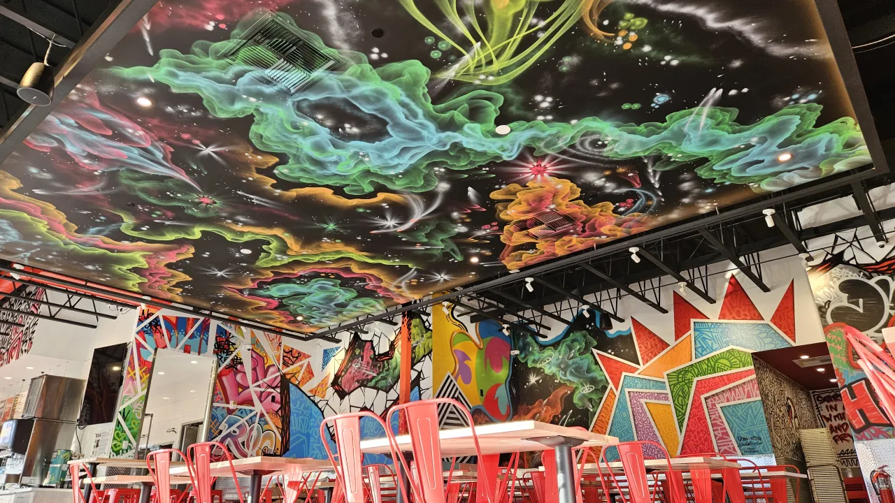 Interior view of Dave's Hot Chicken on Jefferson Rd, Rochester, NY, featuring vibrant ceiling murals and red seating.