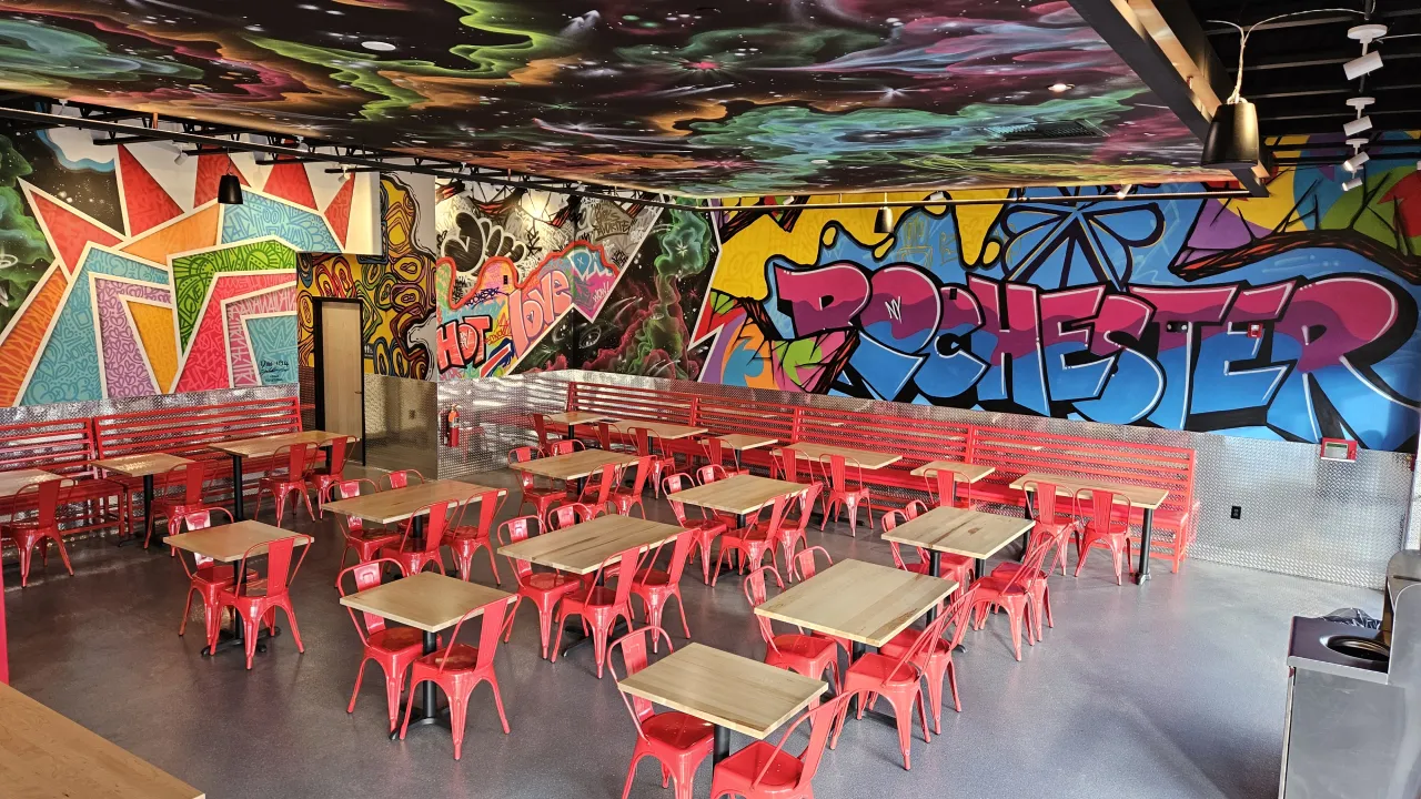 Interior view of Dave's Hot Chicken in Rochester, NY, showcasing vibrant murals and red seating.