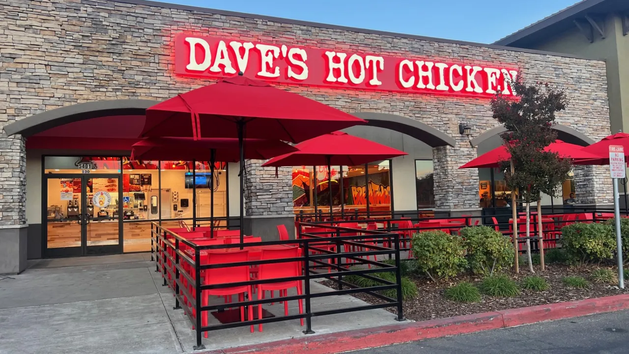 Exterior view of Dave's Hot Chicken on Lone Tree Way in Brentwood, CA, featuring red umbrellas and vibrant signage.