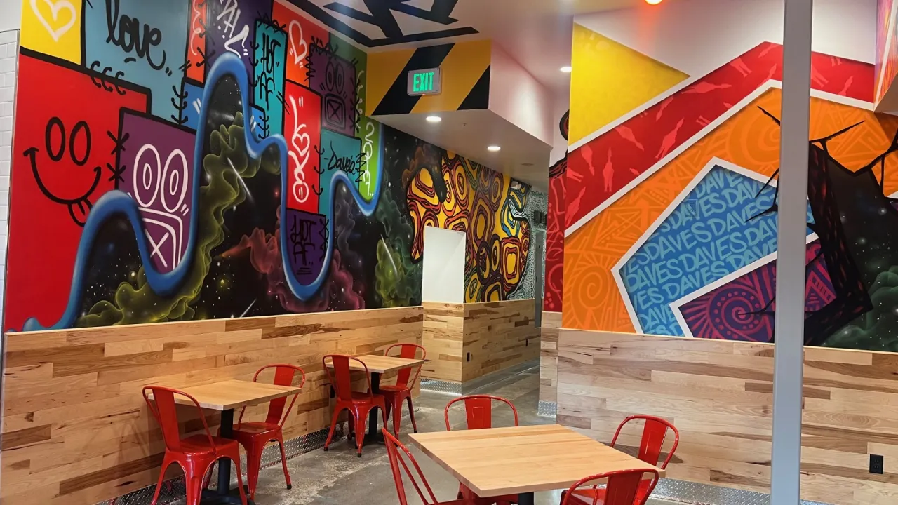 Interior view of Dave's Hot Chicken on Lone Tree Way, Brentwood, CA, showcasing vibrant murals and red metal chairs.