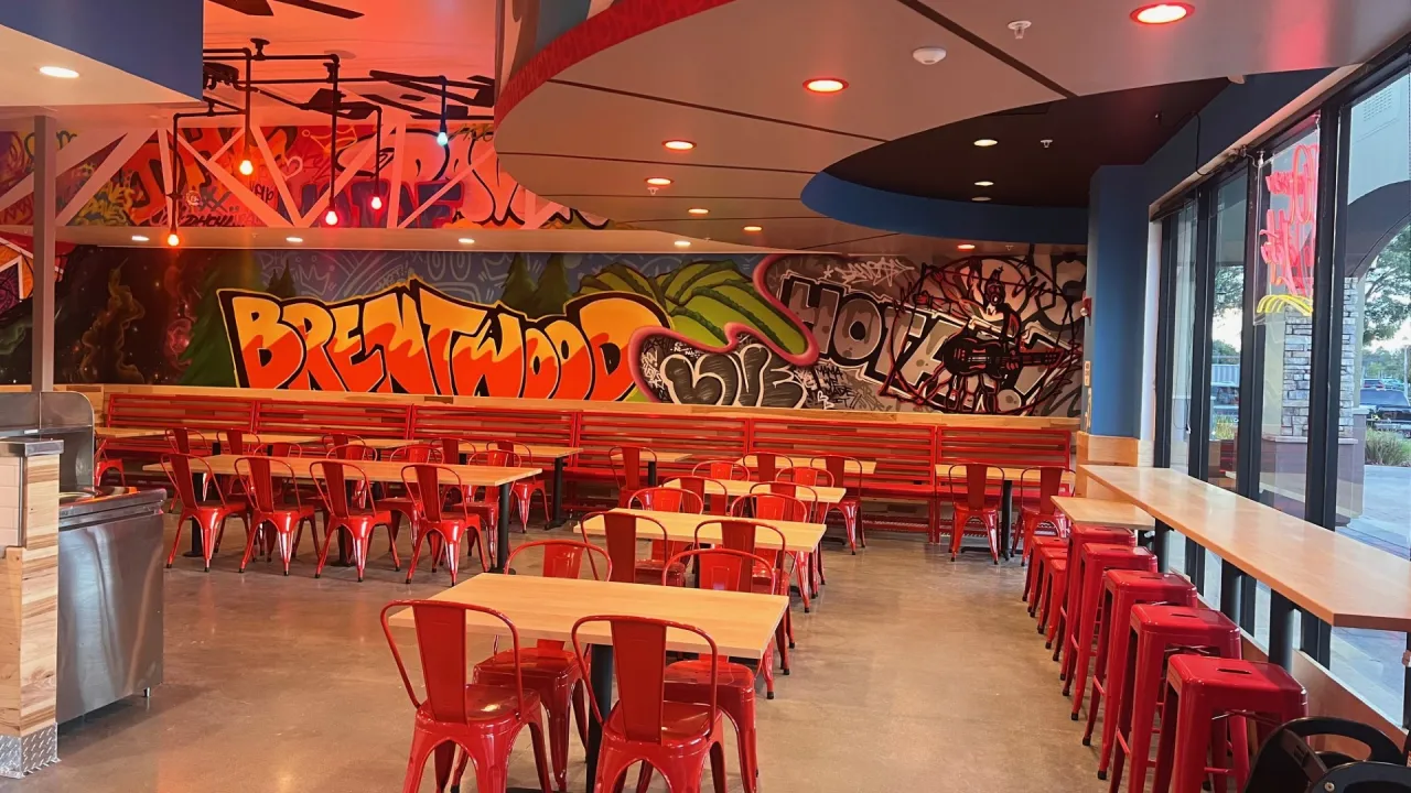 Interior view of Dave's Hot Chicken in, Brentwood, CA, featuring vibrant murals and red seating.