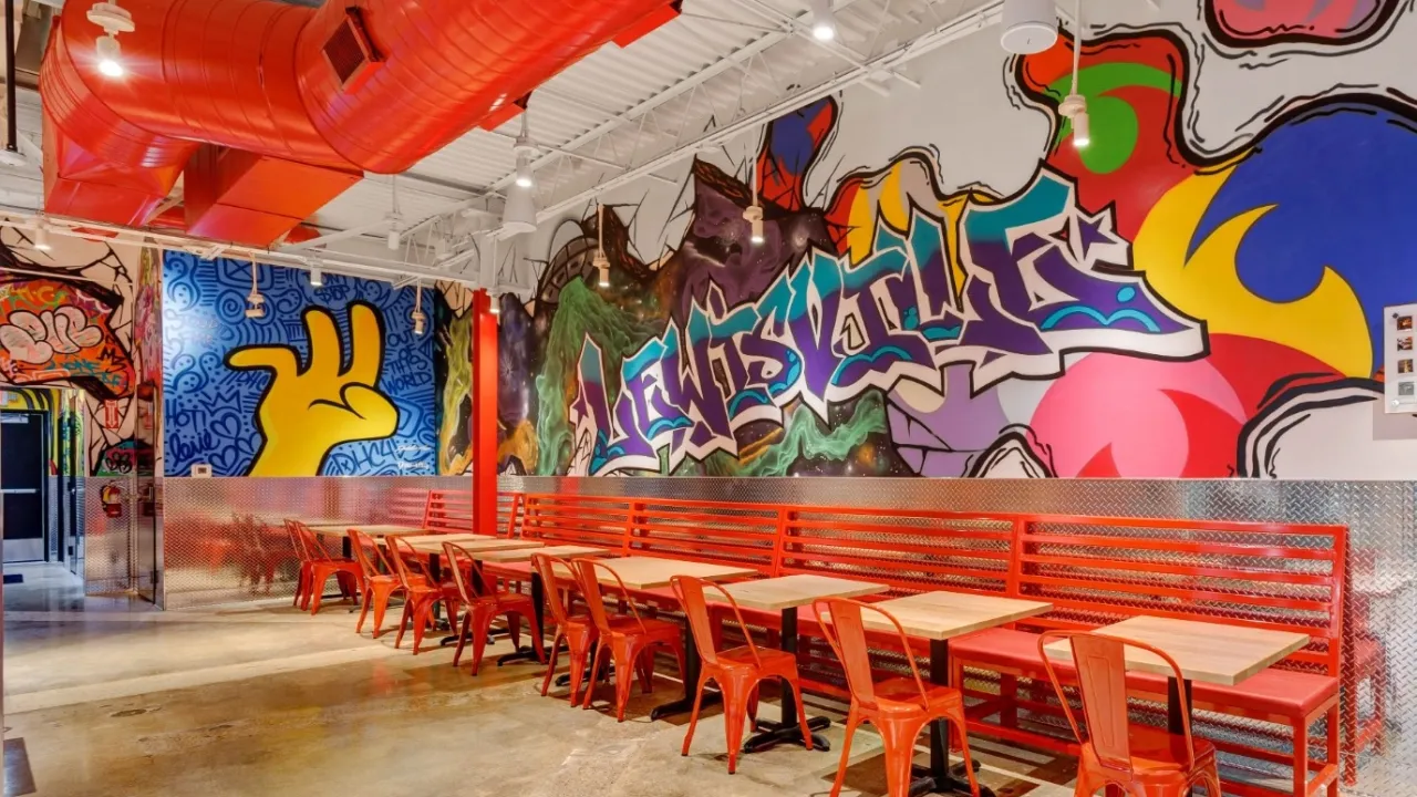 Interior view of Dave’s Hot Chicken featuring vibrant murals and red seating in Lewisville, TX on Main St.