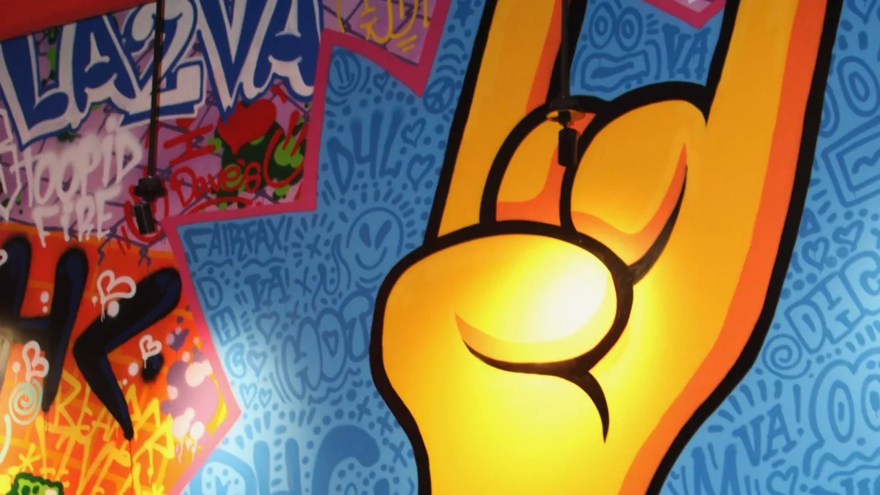 Interior mural at Dave's Hot Chicken on Main Street, Fairfax, VA, featuring graffiti style decor and a rock hand gesture.