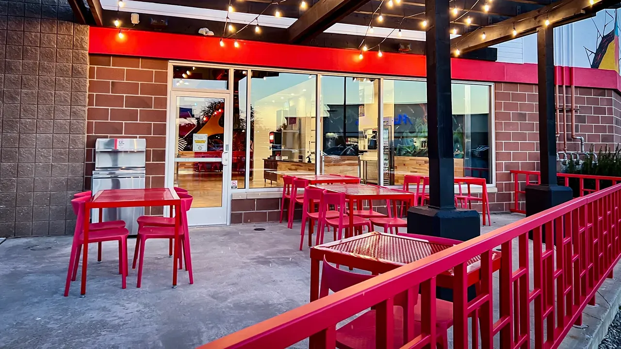 Exterior view of Dave's Hot Chicken on Monroe St, Toledo, OH, showcasing bright red furniture and inviting ambiance.