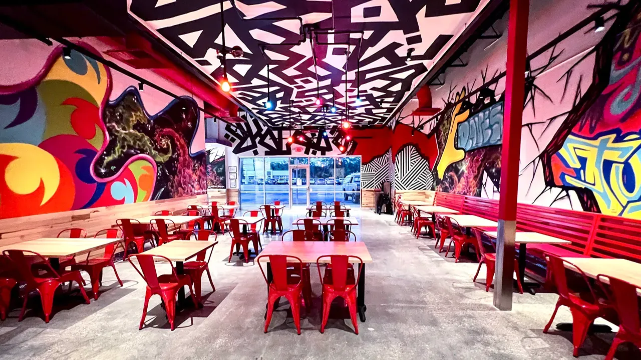 Interior view of Dave's Hot Chicken on Monroe St, Toledo, OH, showcasing vibrant murals and red metal seating.