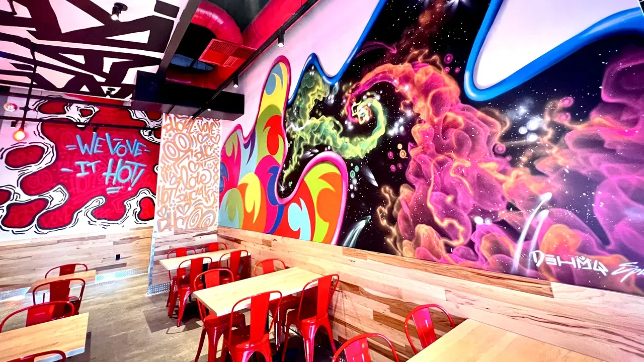 Interior view of Dave's Hot Chicken on Monroe St, Toledo, OH, showcasing vibrant murals and red metal chairs.