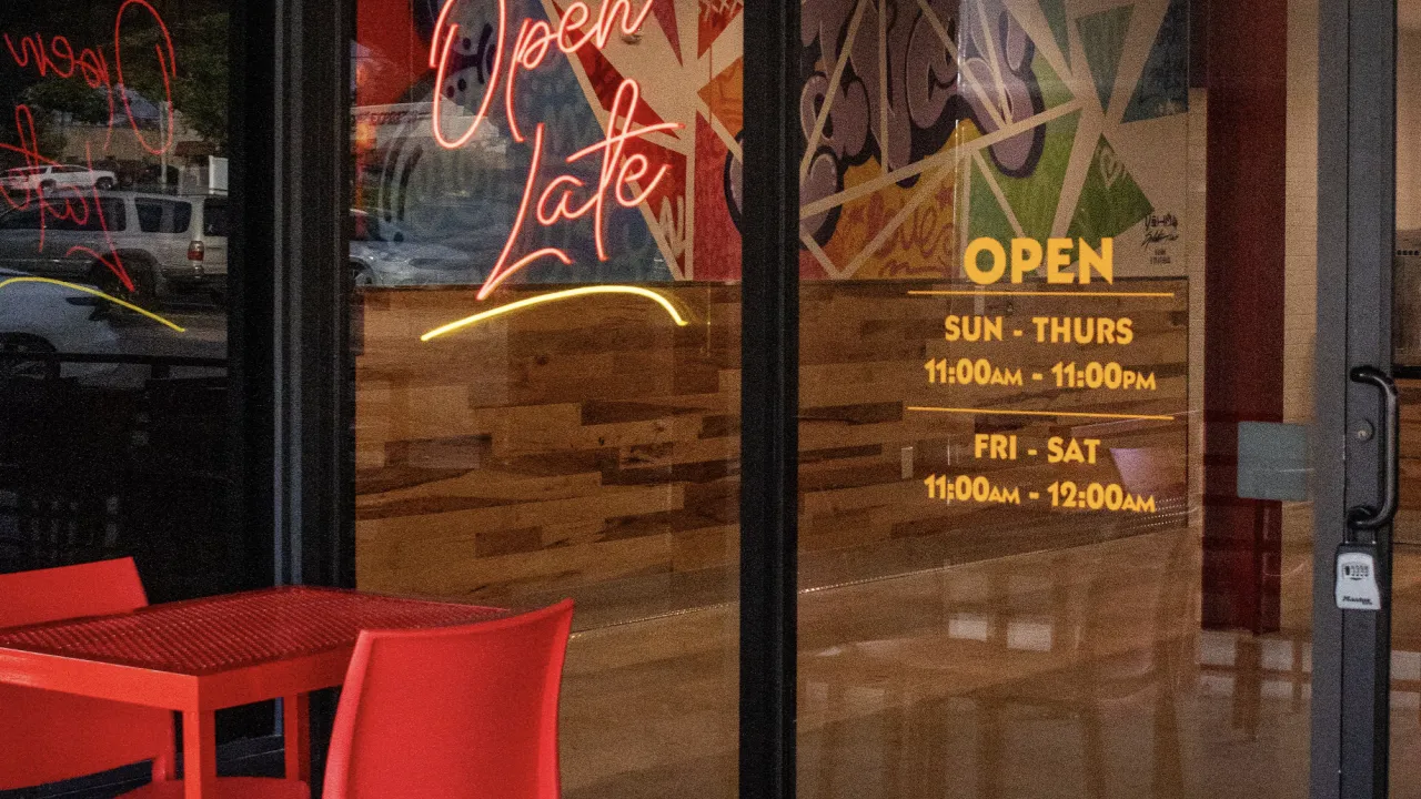 Interior view of Dave's Hot Chicken in Vestavia Hills, AL, showcasing vibrant decor and hours of operation on glass door.