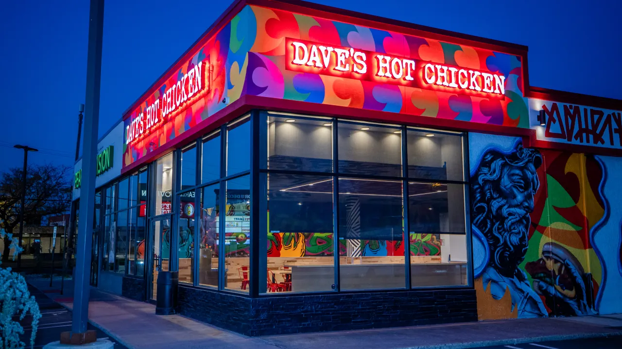 Exterior view of Dave's Hot Chicken on NJ-18, East Brunswick, NJ, showcasing vibrant murals and illuminated signage.