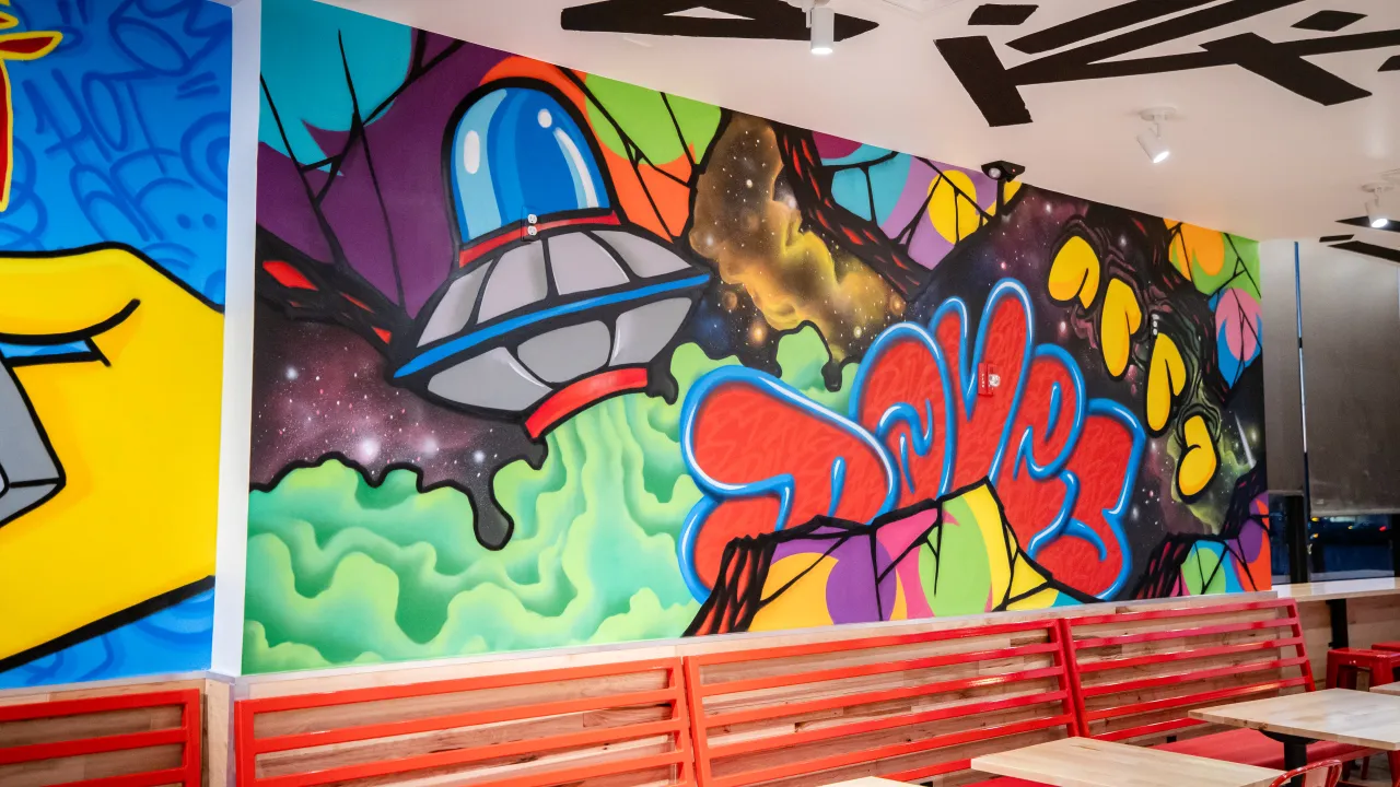 Interior view of Dave's Hot Chicken in East Brunswick, NJ, showcasing vibrant mural art and red seating.