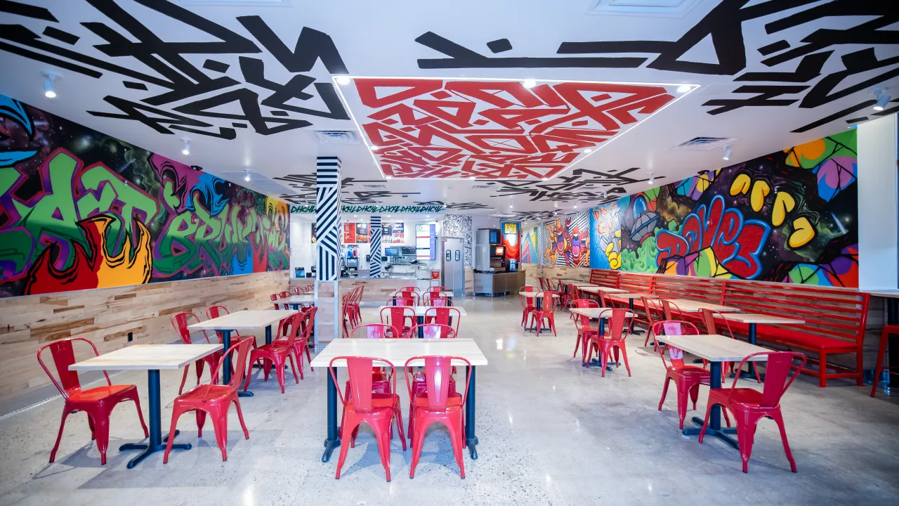 Interior view of Dave's Hot Chicken at 326 NJ-18, East Brunswick, NJ, featuring colorful murals and red seating.