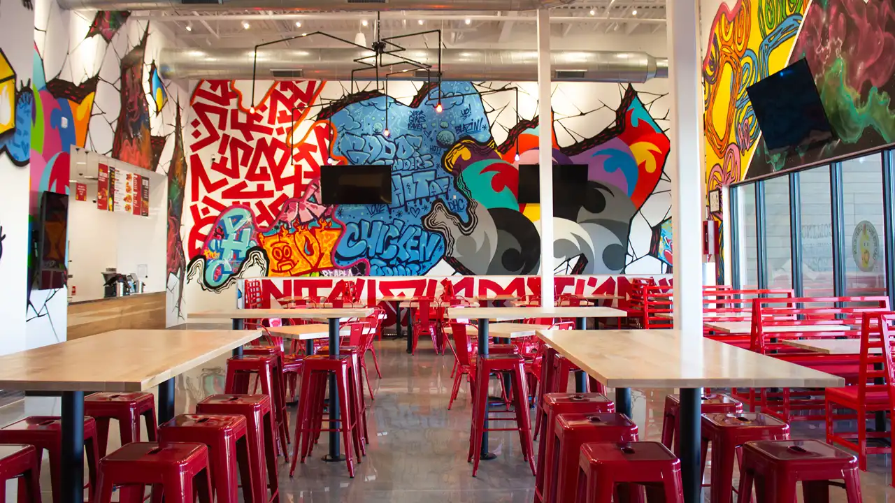 Spacious dining area at Dave’s Hot Chicken in Yukon, OK, with red booth seating, bright murals, and graffiti-covered walls.