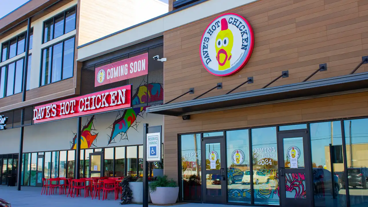 Exterior shot of Dave’s Hot Chicken on NW 10th St, Yukon, OK, featuring a 'Coming Soon sign and outdoor red seating area.