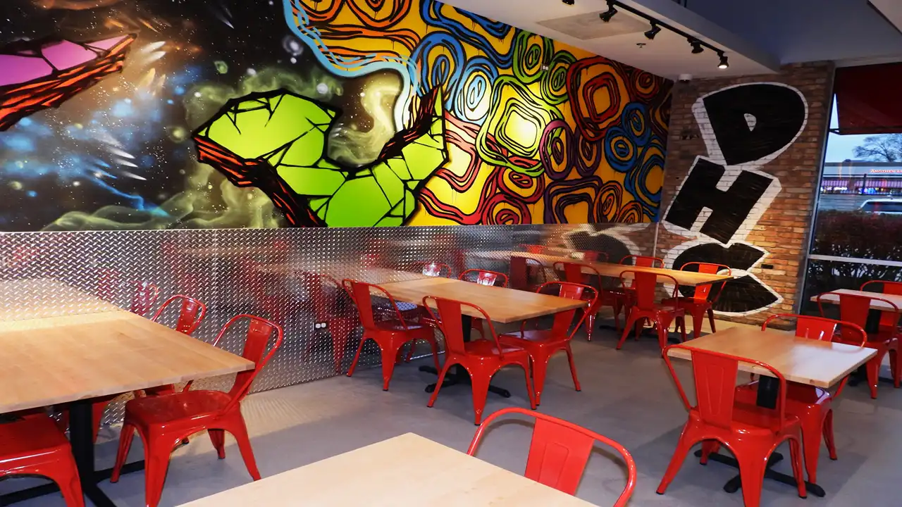 Vibrant wall art featuring green and orange patterns inside Dave’s Hot Chicken on LaGrange Rd, Orland Park, Illinois, with modern red seating.