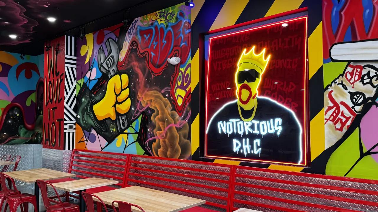 Interior view of Dave's Hot Chicken at 41 Park Ave, Worcester, MA, featuring vibrant murals and red metal seating.