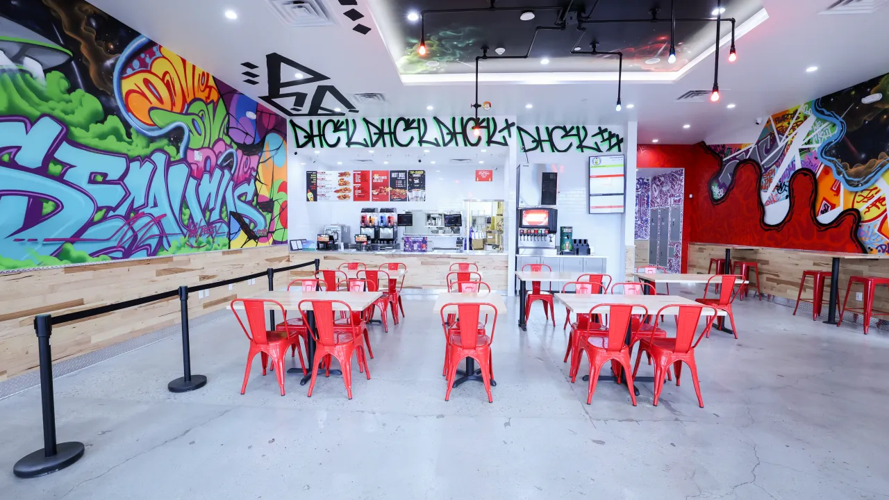 Interior view of Dave's Hot Chicken in Secaucus, NJ, showcasing vibrant murals and red seating.