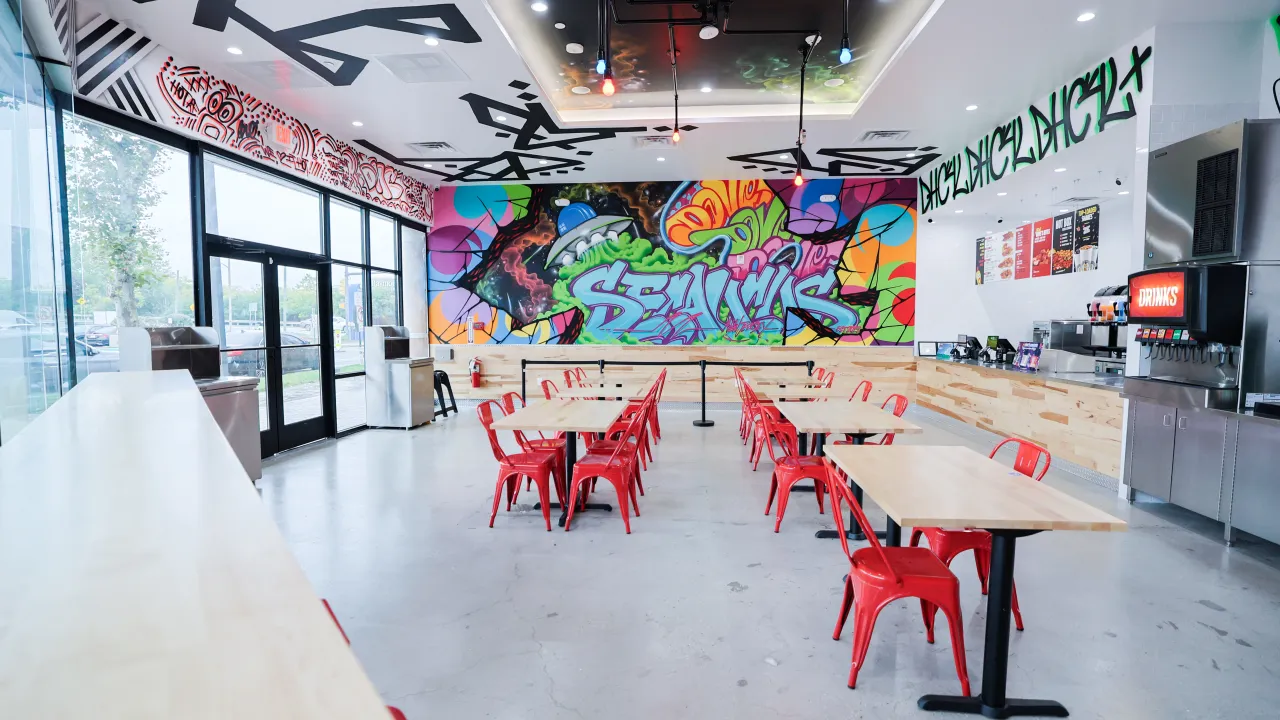 Interior view of Dave's Hot Chicken in Secaucus, NJ, showcasing vibrant murals, red seating and large windows.